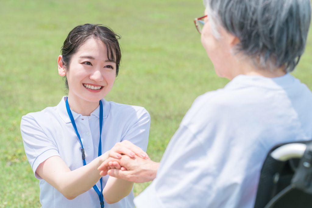 笑顔で高齢者と手を握る介護士